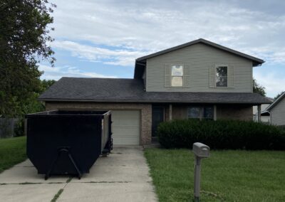 Large black dumpster parked in a suburban driveway.