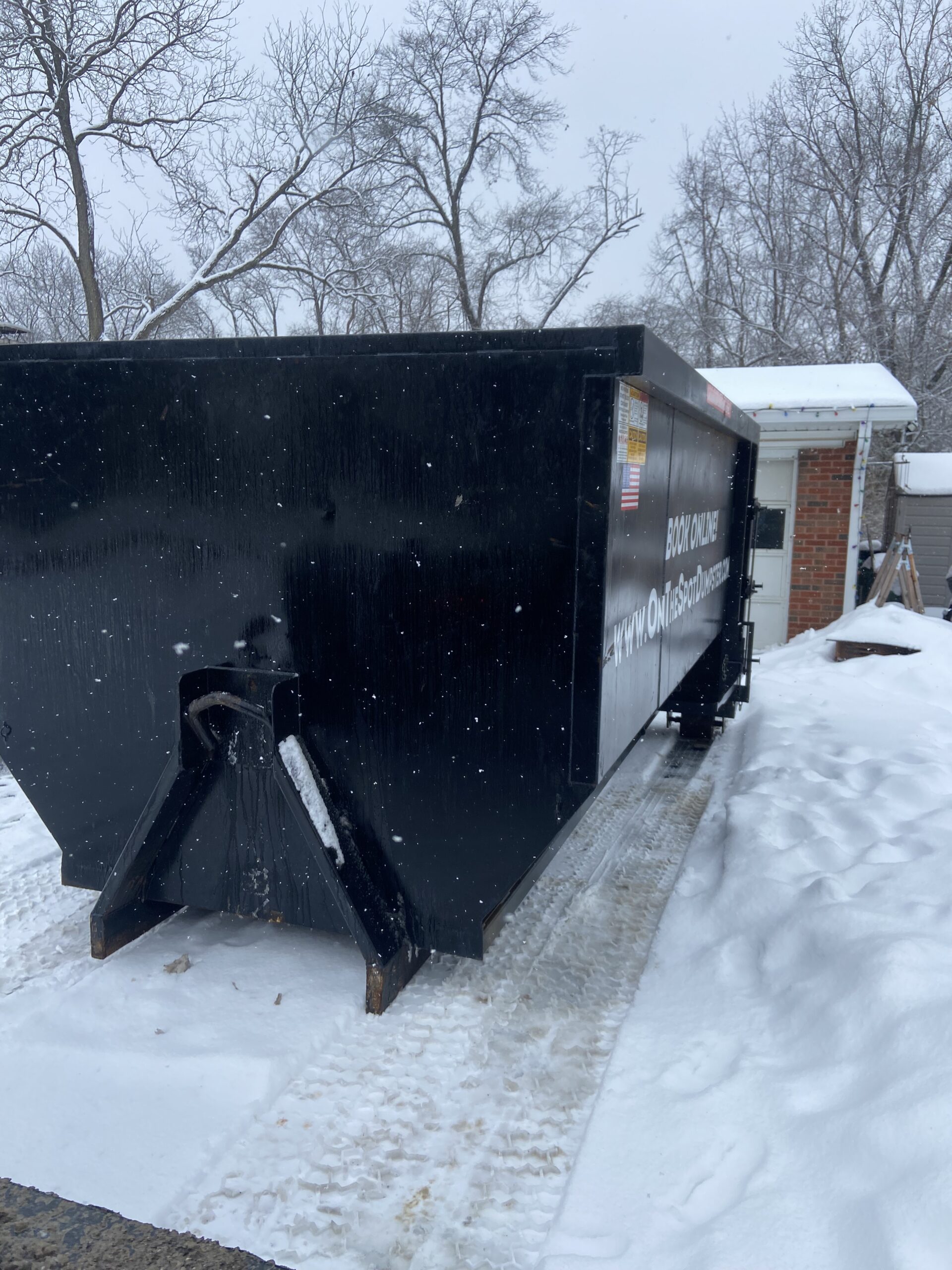 Large black dumpster on a snow-covered driveway.